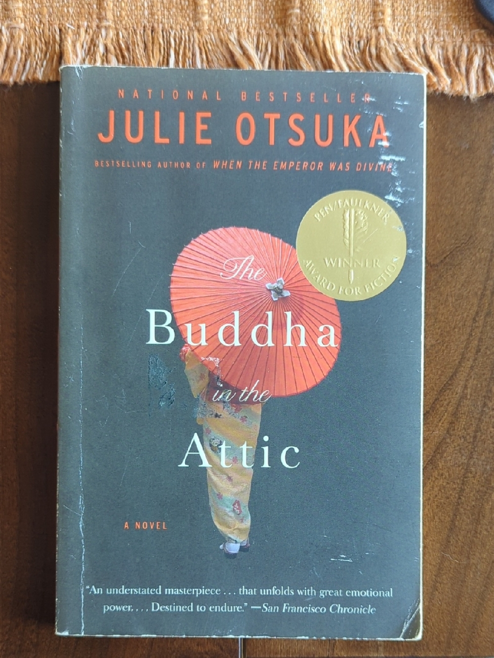 The Buddha in the Attic by Julie Otsuka - Dark Gray Cover with Red Umbrella